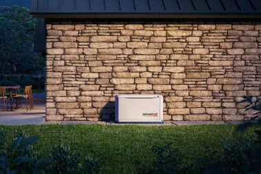Home standby generator installed on a pad beside a stone wall